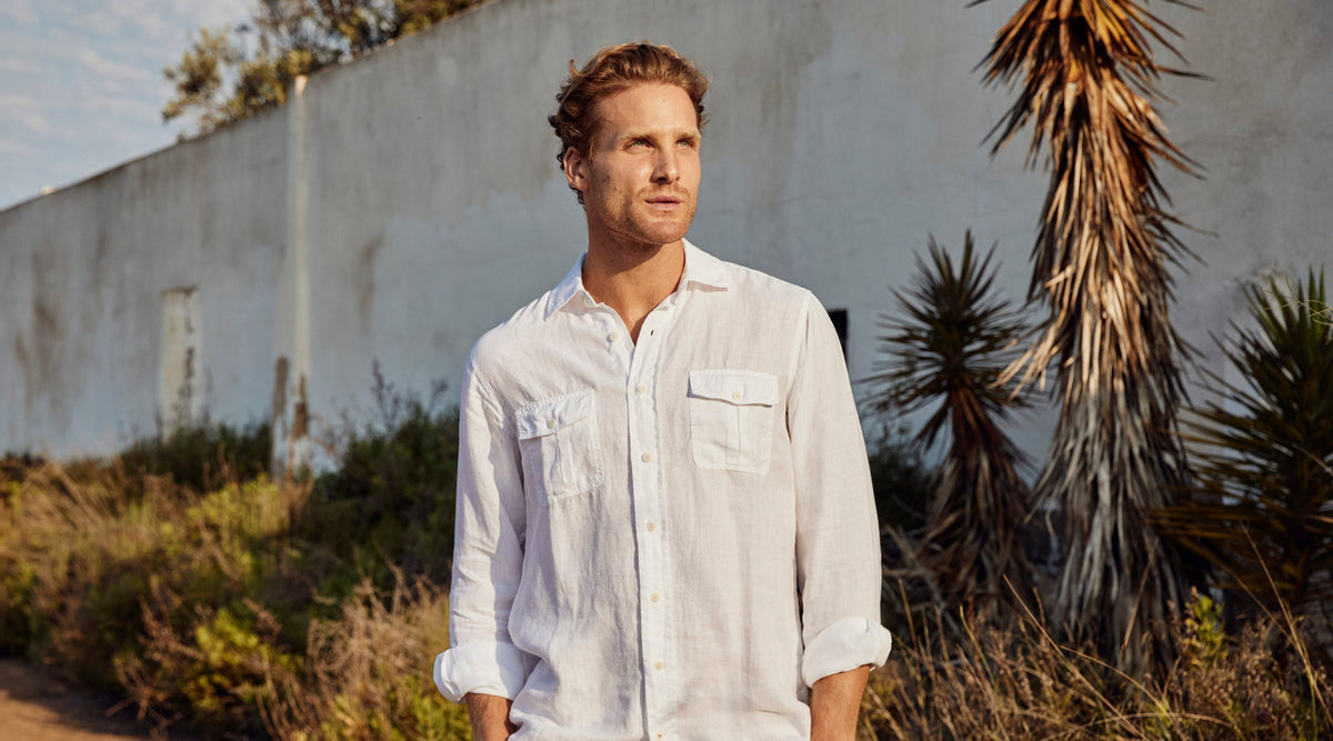 Man wears a white hemp shirt against a white wall with tropical plants