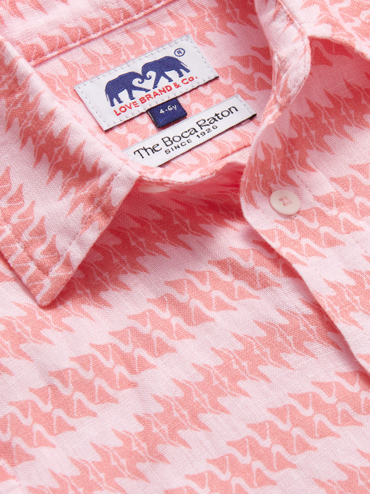 Close-up of the Boys Roseate Spoonbill Abaco Linen Shirt by LOVE BRAND & Co. featuring a pink bird pattern and labels near the collar.