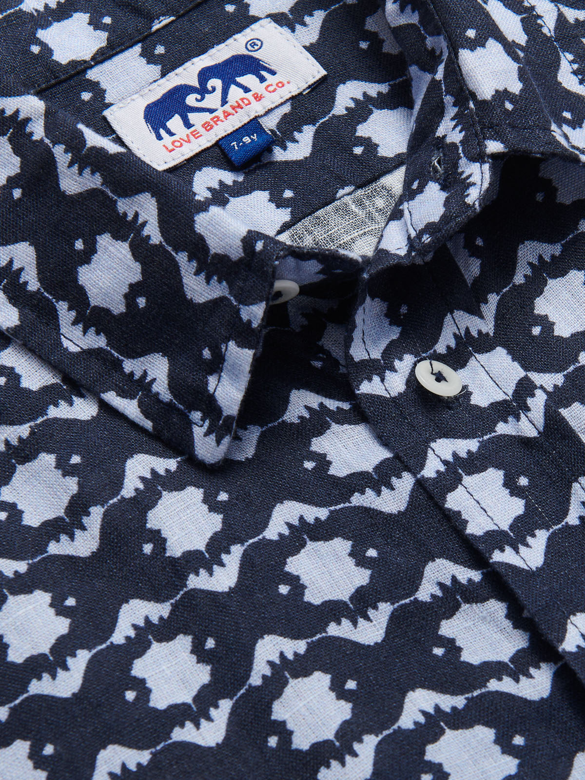 Close-up view of Boys Rhino Rhythm Abaco Linen Shirt showcasing a geometric print featuring hidden rhinos in navy and sky blue, inspired by African conservation efforts.