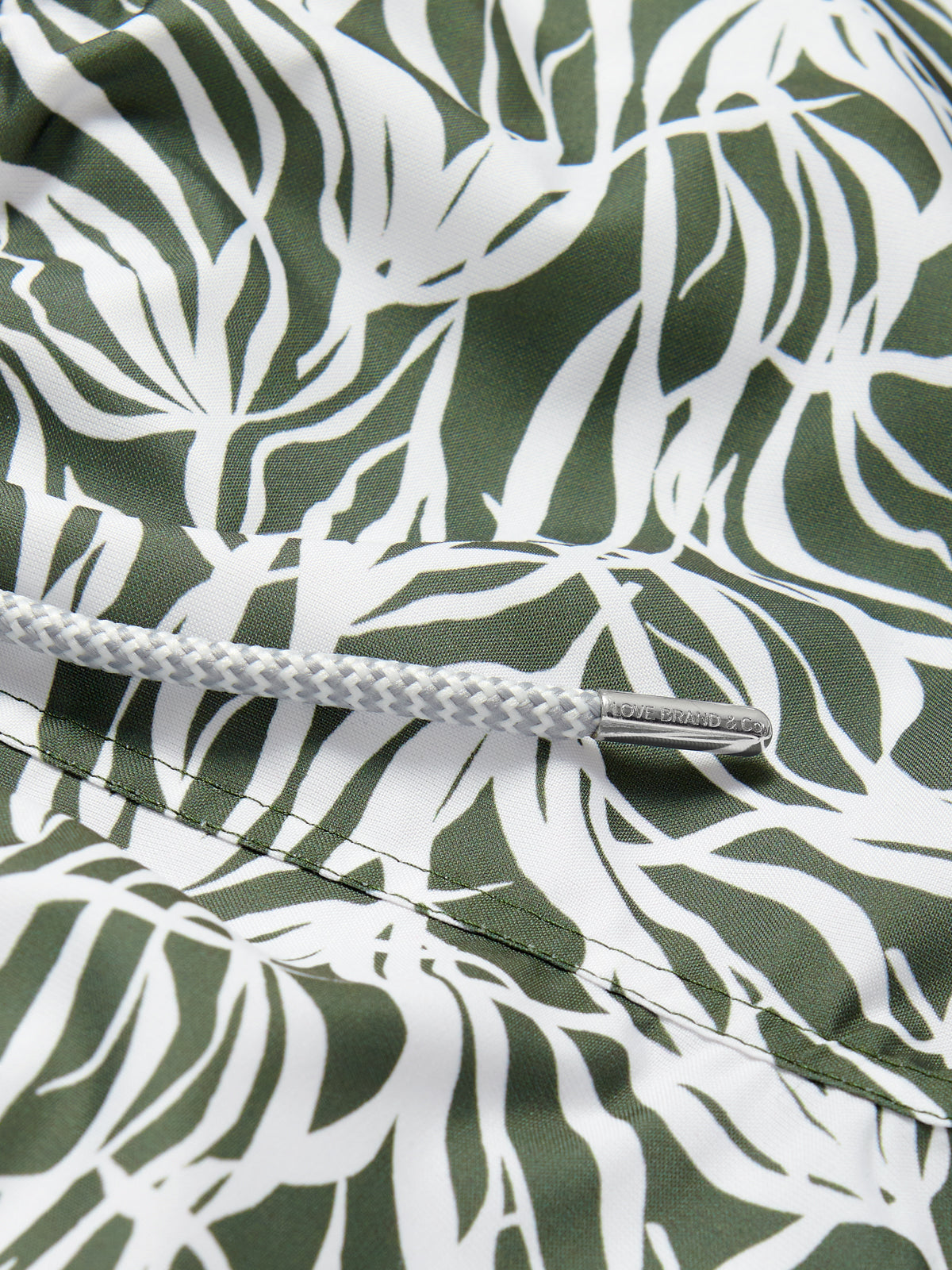 Close-up view of Men's Talamanca Bay Staniel Swim Shorts in olive green with white sea grass pattern, featuring quick-dry recycled fabric and braided drawstring.