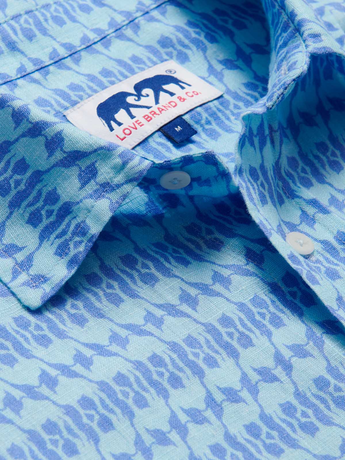 Close-up image of the Camel Mirage Sky Abaco mens Linen Shirt. Old money shirt showing its blue and turquoise patterned fabric and button details with a visible "Love Brand & Co." label.