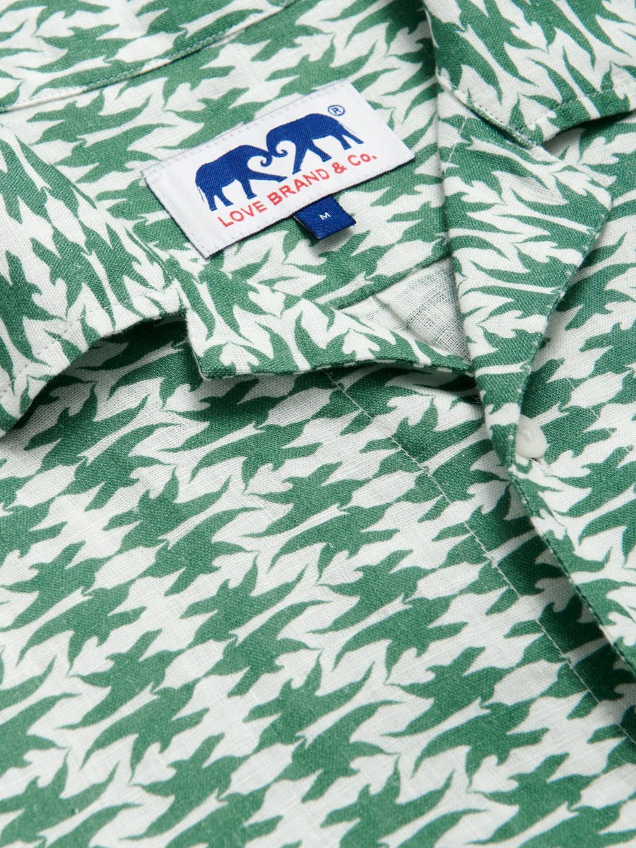 Close-up view of Men's Dolphins of Greece Arawak Linen Shirt featuring a green and white dolphin pattern. Men's linen shirt with a camp collar, and a chest pocket, with the Love Brand & Co. tag visible.
