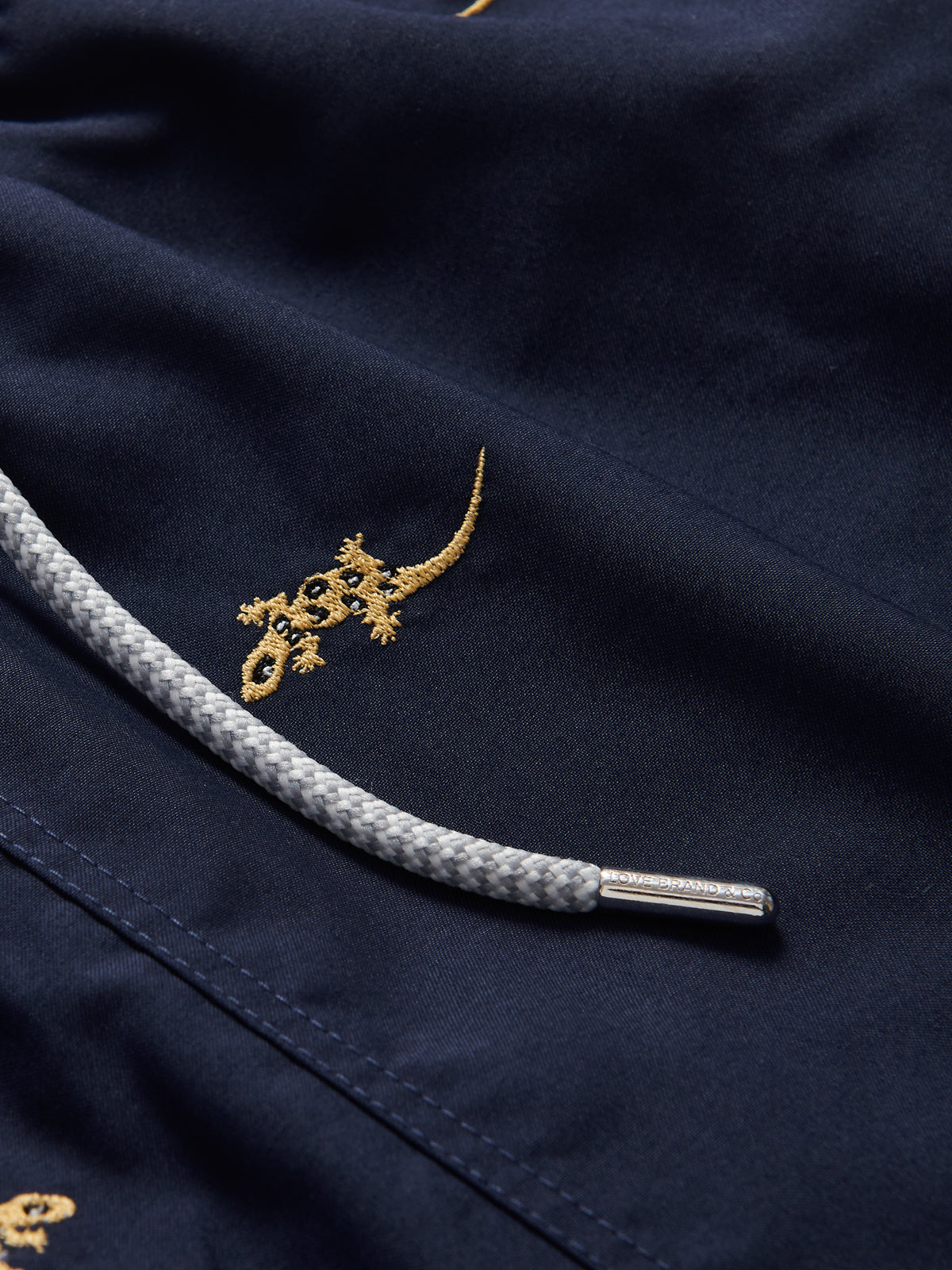 Close-up of gold embroidery detail on Off The Wall Embroidered Staniel Swim Shorts showcasing the Union Island Gecko.