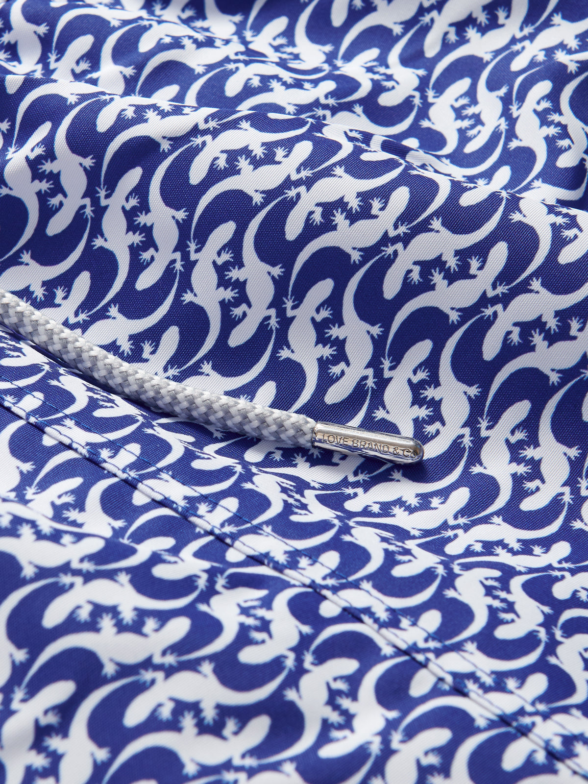 Close-up view of Gecko Island Staniel Swim Shorts. Blue swimming shorts with a white gecko pattern.