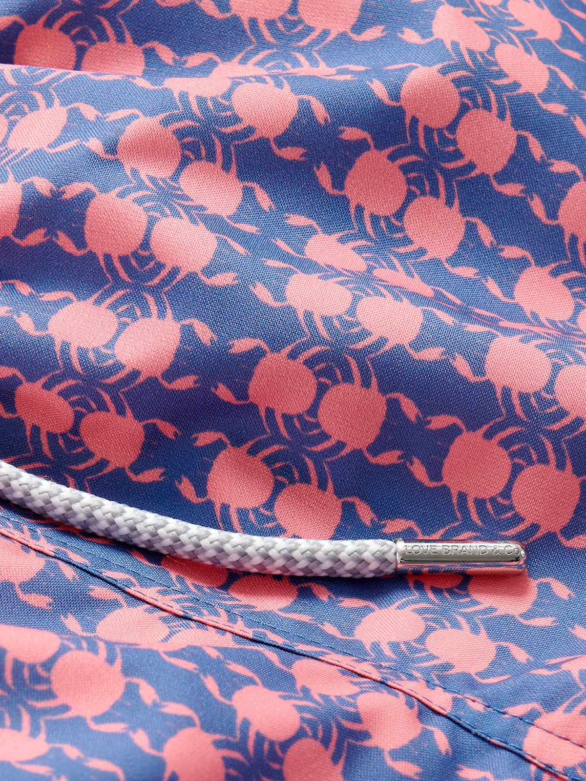 Close-up of Boys Crab Pool Staniel Swim Shorts featuring pink crab and watermelon pattern on a deep blue background with a white drawstring.
