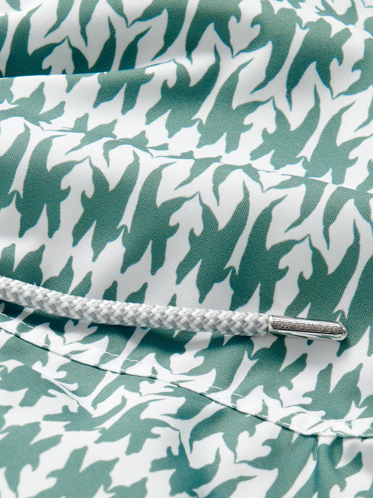 Close-up of Boys Dolphins of Greece Staniel Swim Shorts featuring green and white dolphin pattern and a white drawstring with an engraved nickel-free terminal.