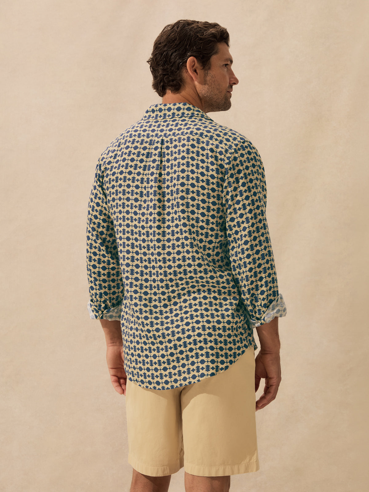 A man shown from the back wearing a long-sleeve button-up shirt with a blue and beige geometric pattern.