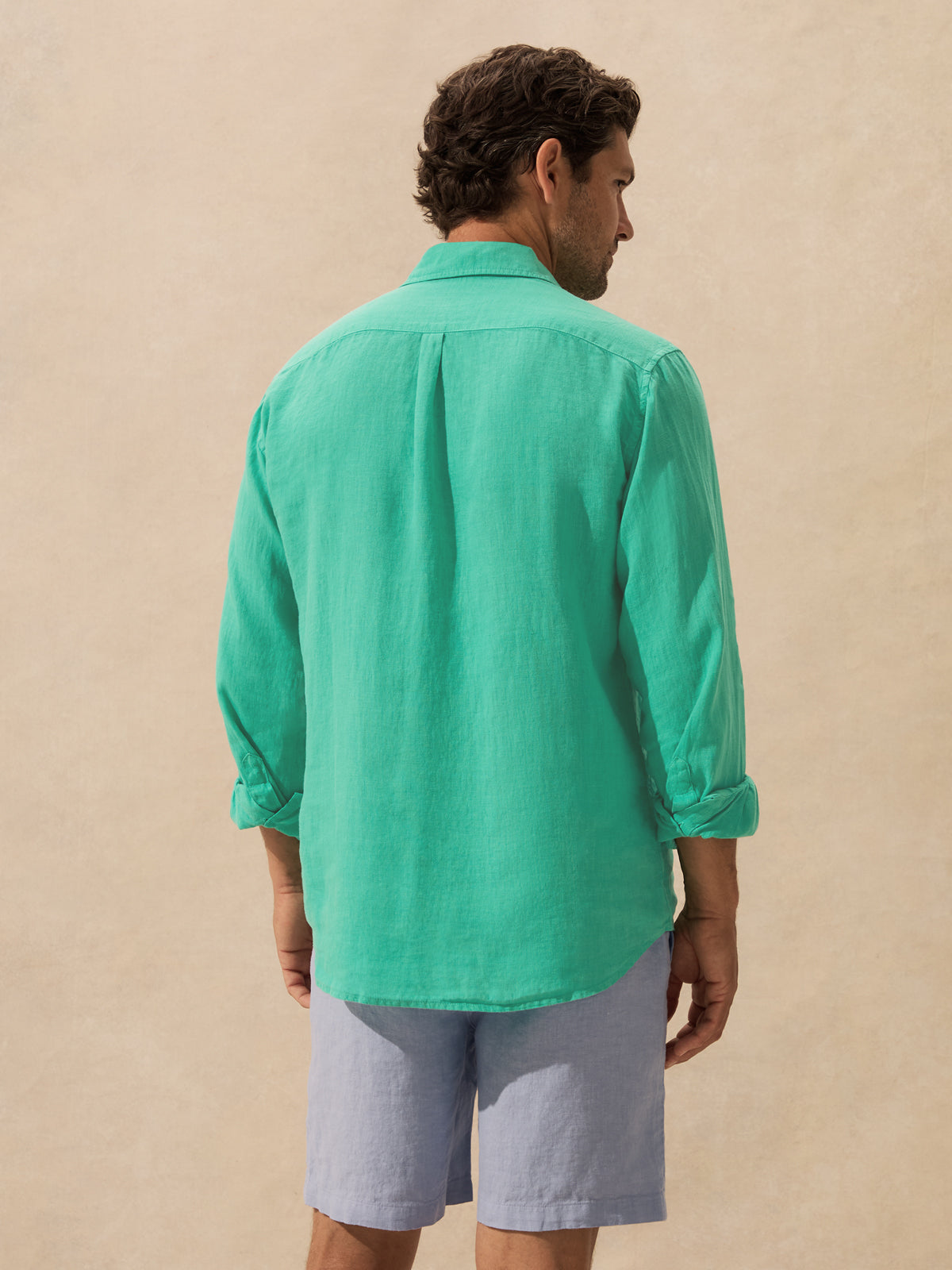 A man shown from the back wearing a mint green long-sleeve linen shirt against a textured beige background.
