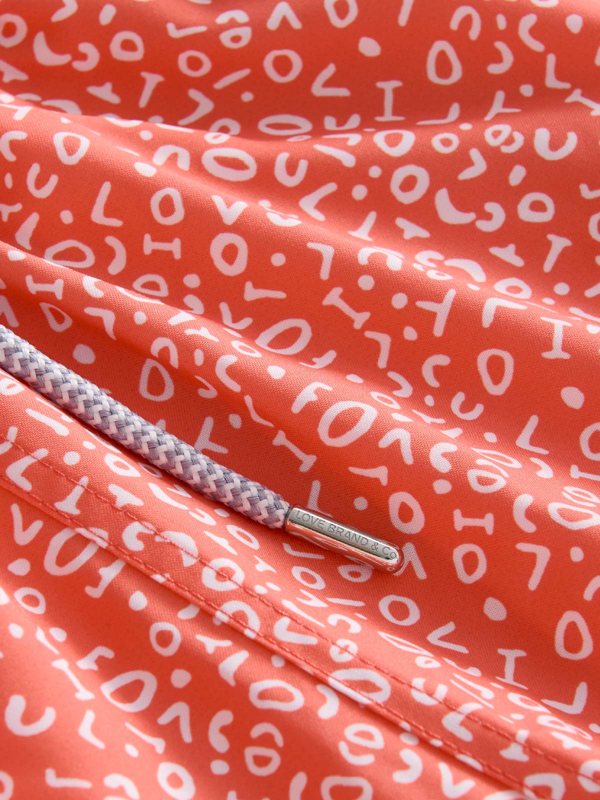 Close-up of red swim shorts fabric with white patterns and a drawstring