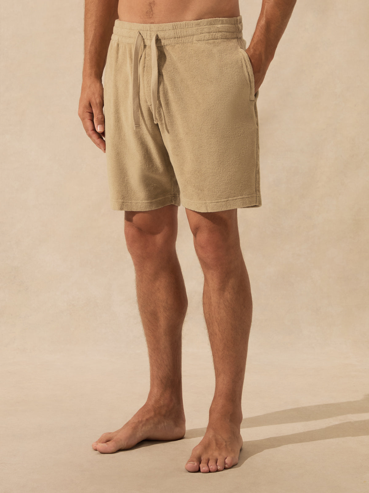 Beige drawstring shorts worn by a model, shown from the waist down against a matching beige textured studio backdrop.