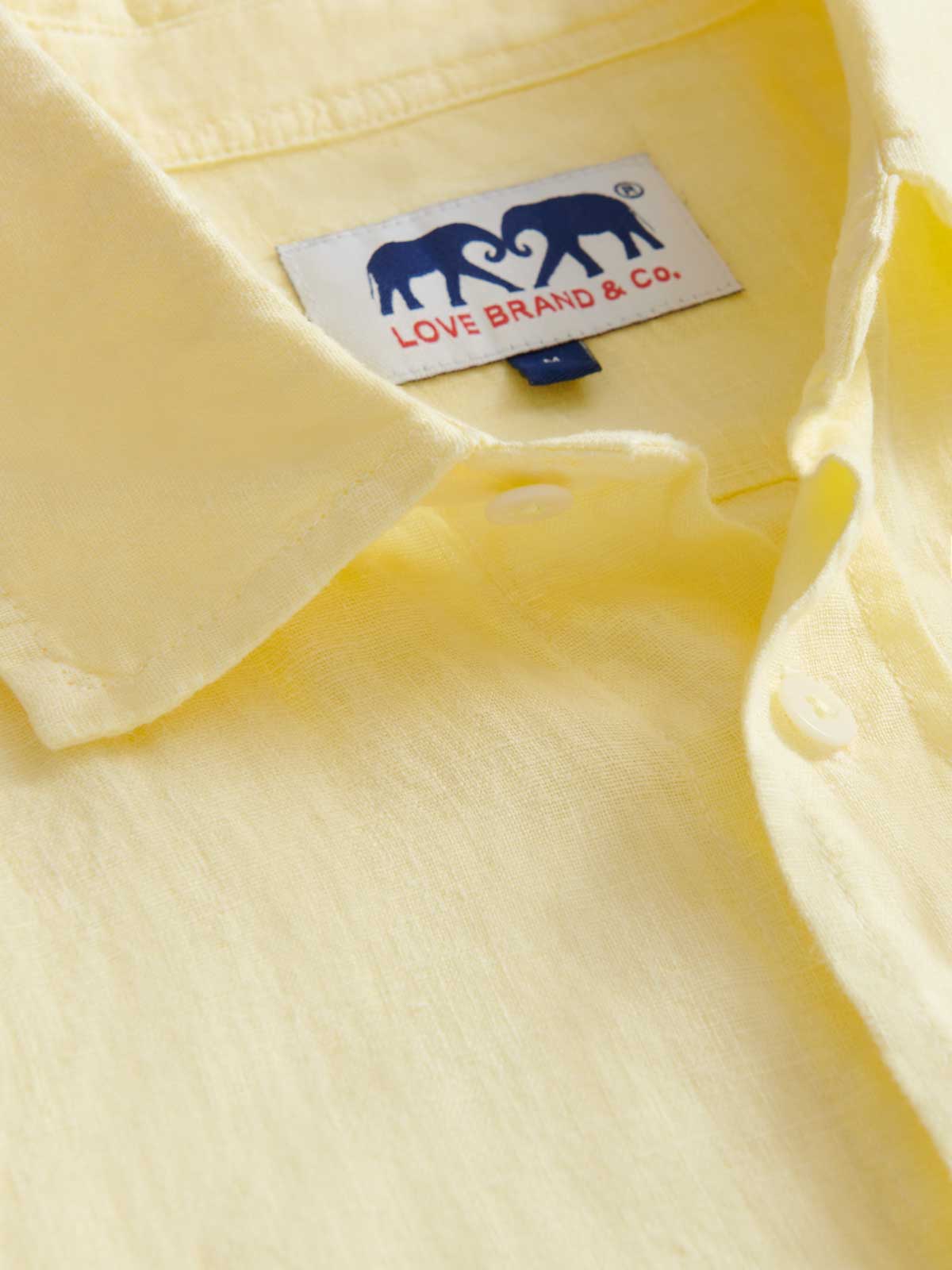 Close-up view of the collar of the yellow linen shirt by love brand showcasing the brand logo and linen material.