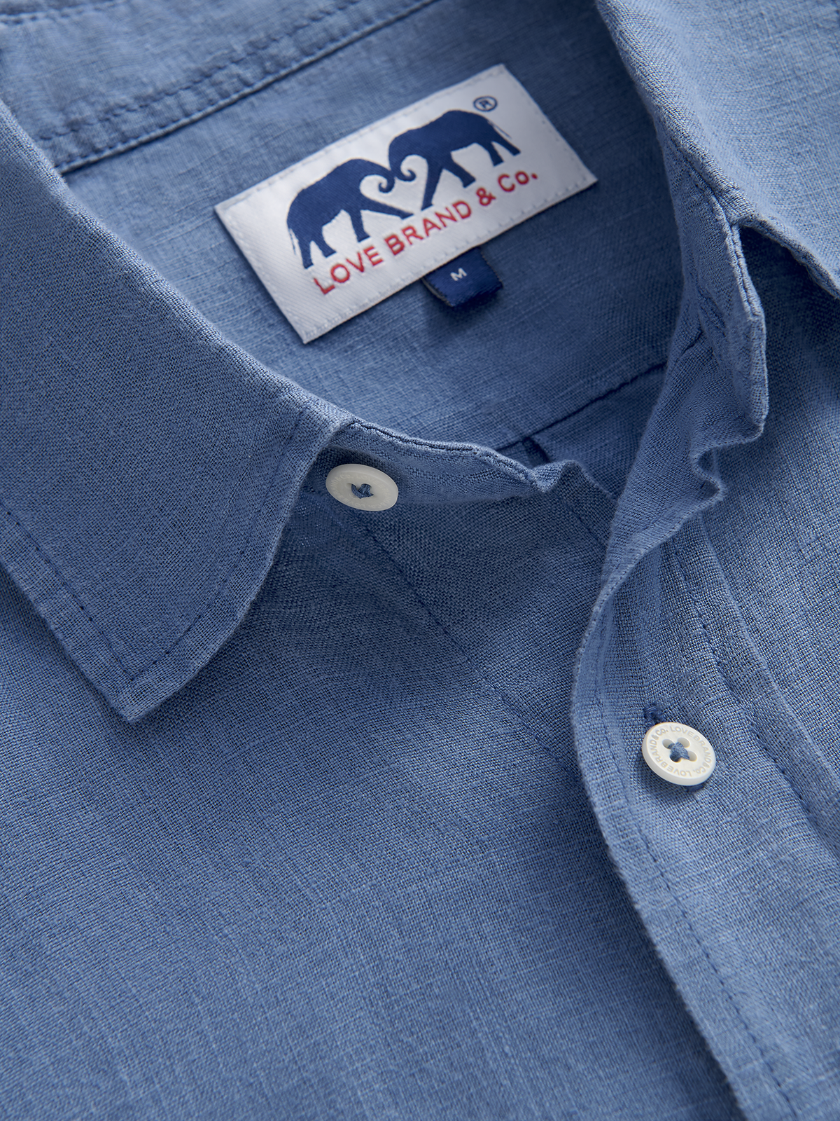 Close-up of a blue shirt with a brand label featuring two elephants and 'Love Brand & Co.' text.