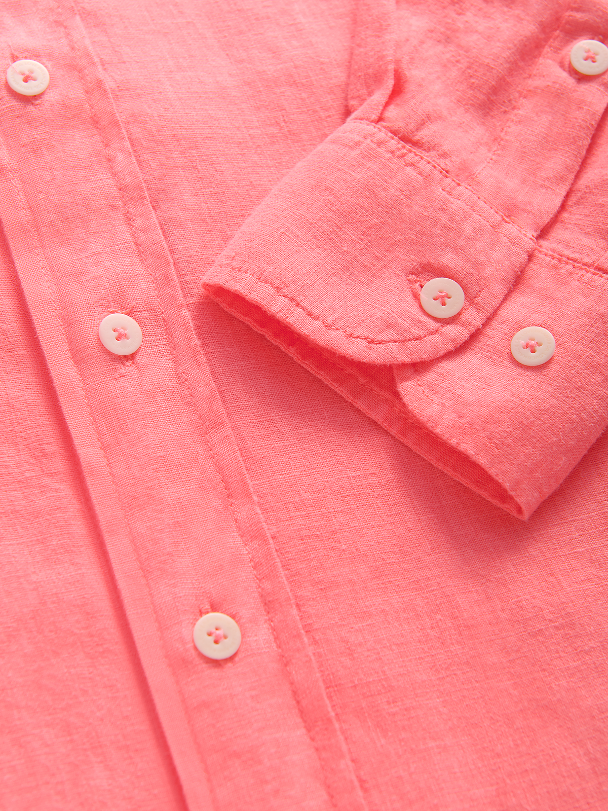 Close-up of a pink linen shirt with buttons and a sleeve cuff.