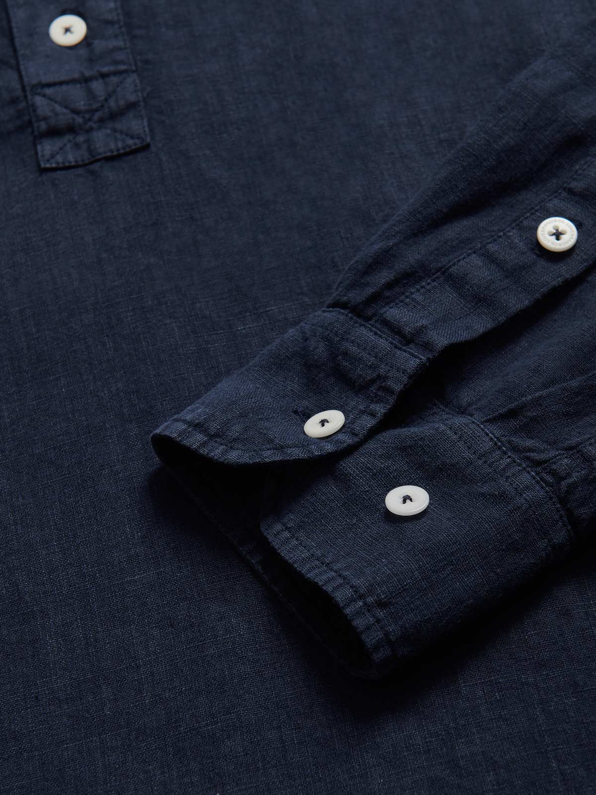 Close-up view of Men's Navy Blue Hoffman Linen Shirt. Navy blue linen shirt with long sleeves and half-button-up design. Detailed view of cuffs with corozo nut buttons.