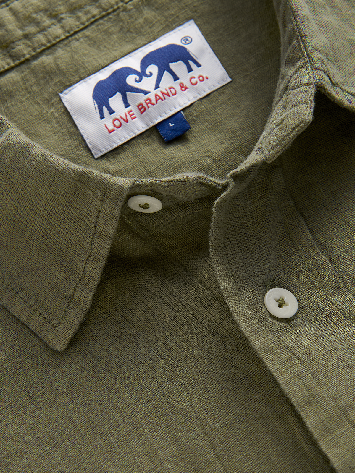 Close-up of an olive green shirt collar with a visible love brand label featuring two elephants and text.