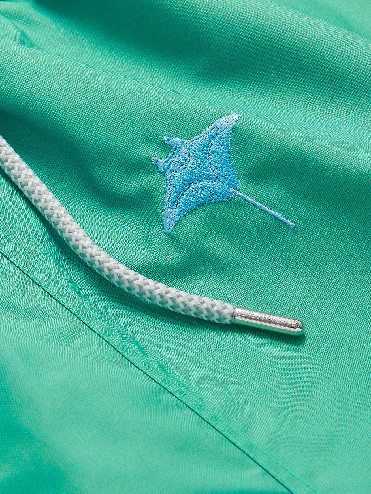 Close-up of the Men's Manta Migration Embroidered Staniel Swim Shorts showcasing the detailed manta ray embroidery on lightweight green fabric with a braided drawstring.