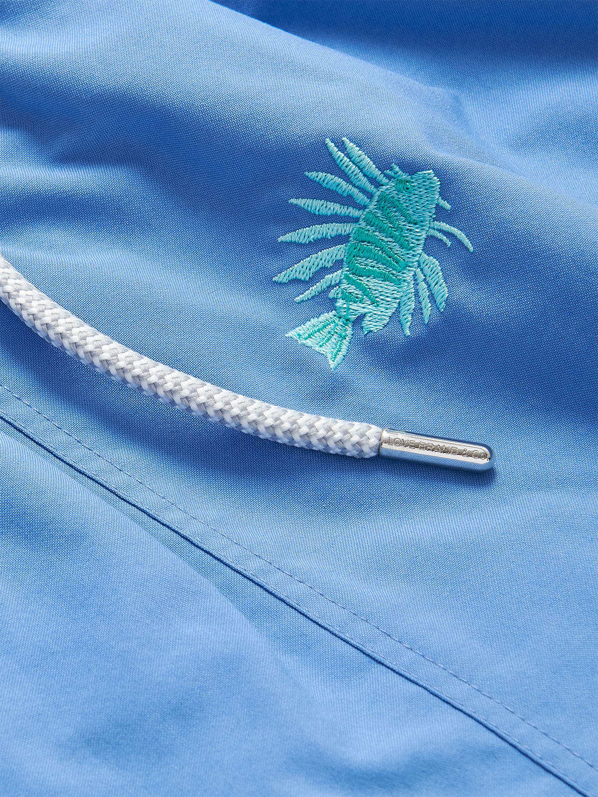 Close-up view of the Boys Fish Fry Embroidered Staniel Swim Shorts featuring an embroidered lion fish pattern on a deep blue fabric with a white drawstring.