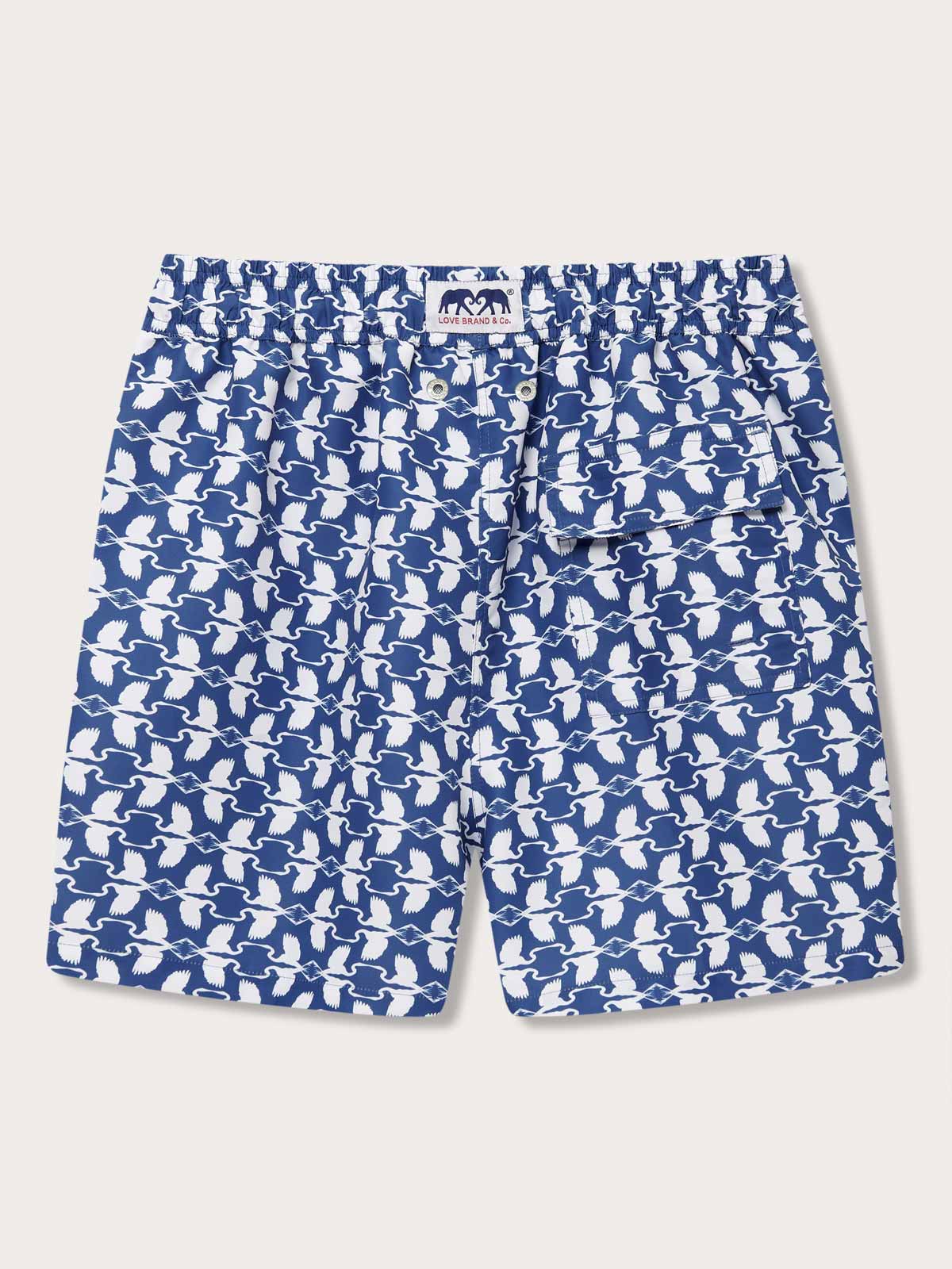 Men's White Heron Staniel Swim Shorts by LOVE BRAND & Co. Patterned swim shorts featuring a pattern of white herons on blue background, made from 100% recycled plastic.