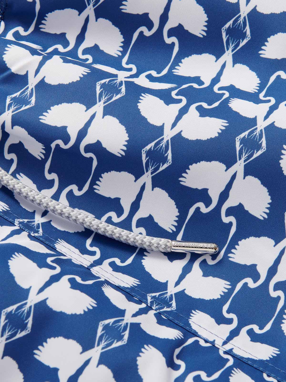 Close-up view of the Men's White Heron Staniel Swim Shorts. Patterned swim shorts showcasing a detailed pattern of white herons on a deep blue background. The image highlights the intricate design and high-quality fabric made from recycled plastic.