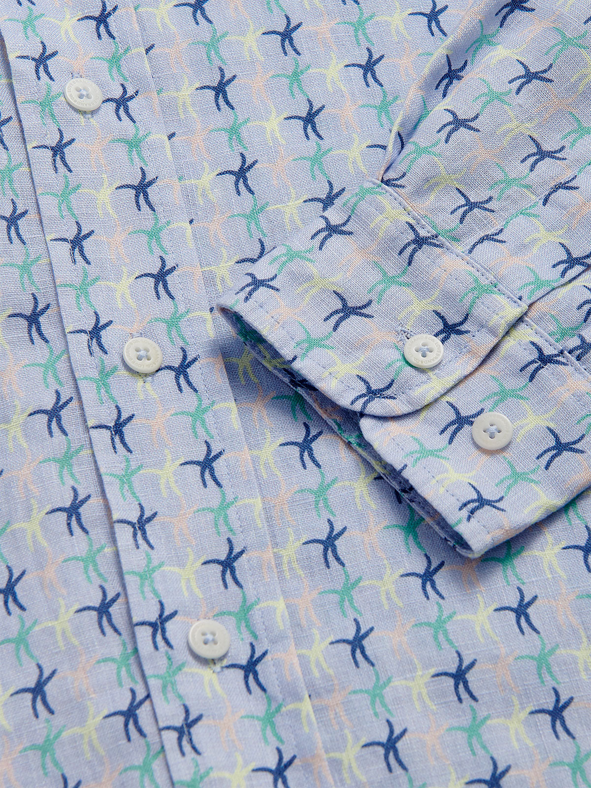 Close-up view of the Men's Star Dancer Abaco Linen Shirt showcasing sea star motifs in pastel pink, limoncello, cay green, and deep blue on an ocean blue background.