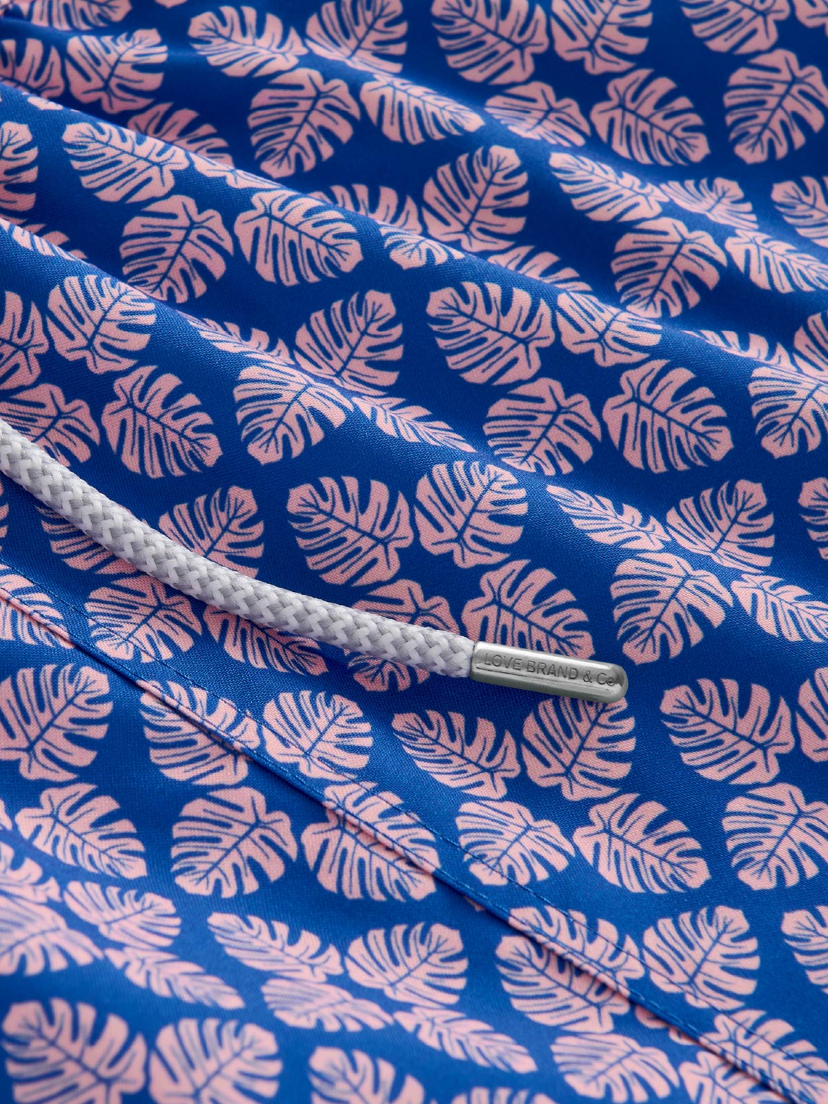 Fabric with pink monsterra leaf pattern on a blue fabric.