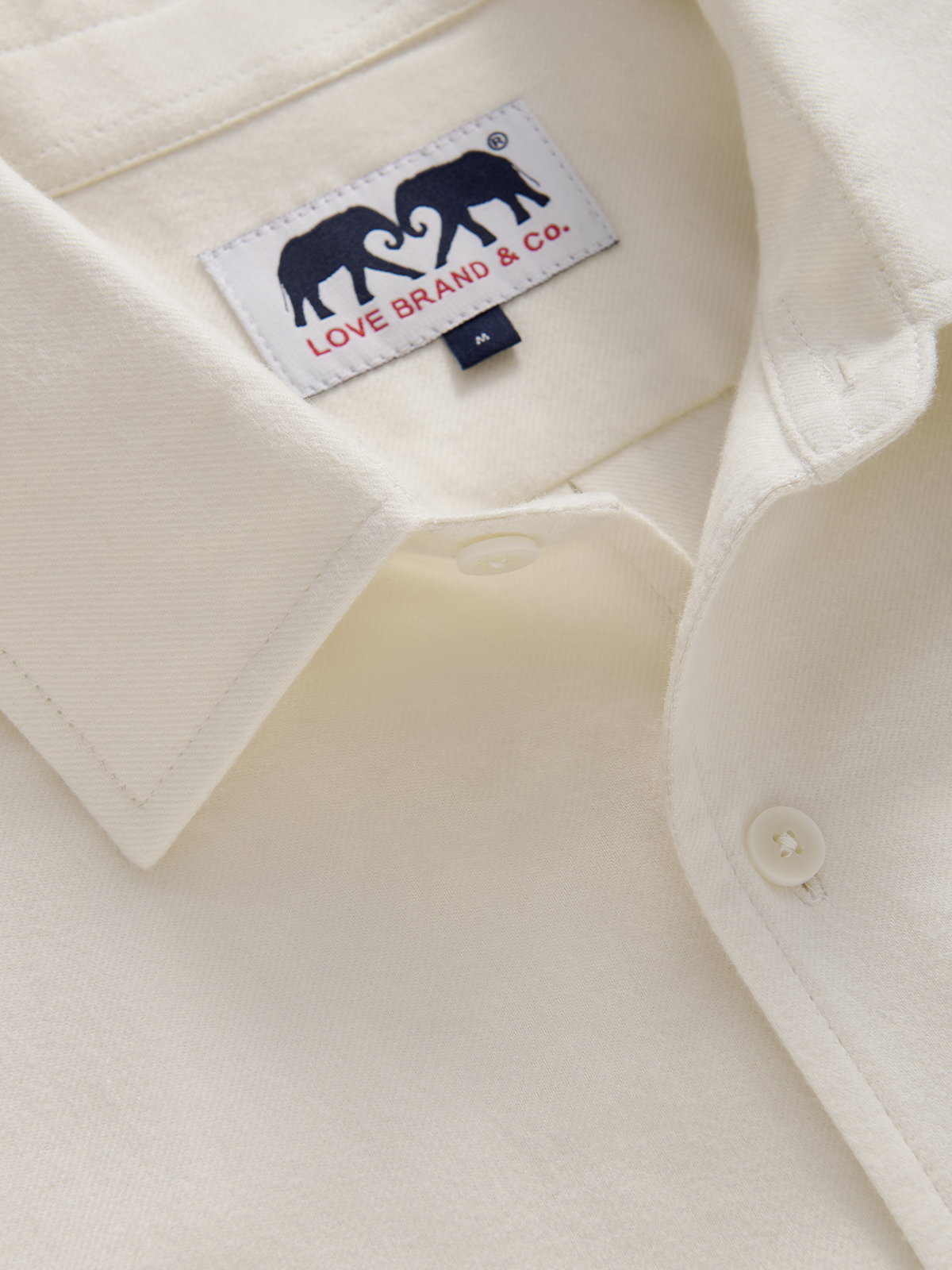Close-up of a cream-coloured button-down shirt collar showing the Love Brand & Co. woven label with two navy elephant logos.