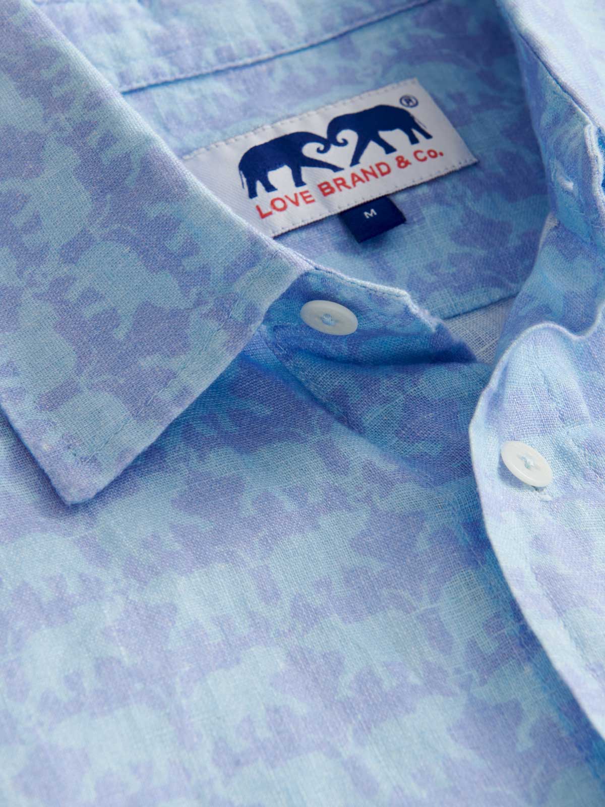Close-up view of mens sky blue linen shirt showcasing elephant pattern.