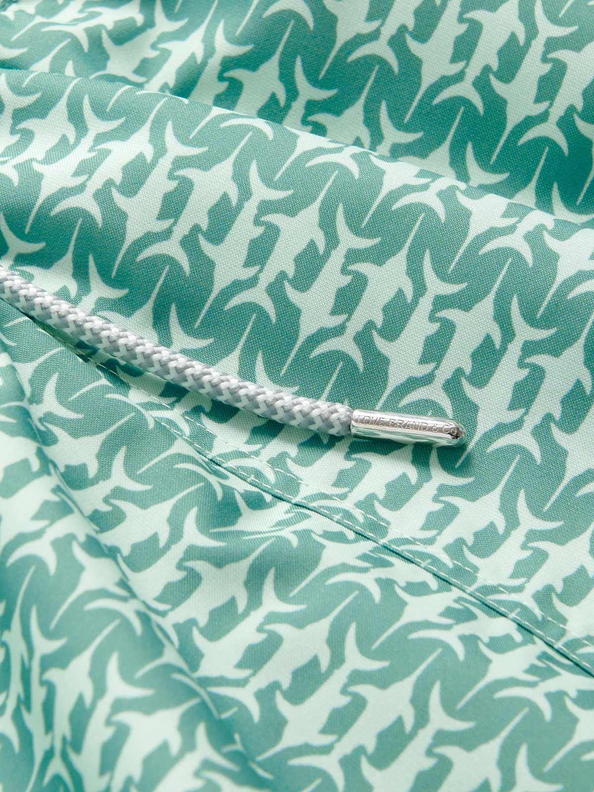 Close-up view of Men's Angarde Staniel Swim Shorts, featuring a swordfish pattern in soft green hues. Image of patterned swim shorts with a focus on the quality fabric and drawstring detail.
