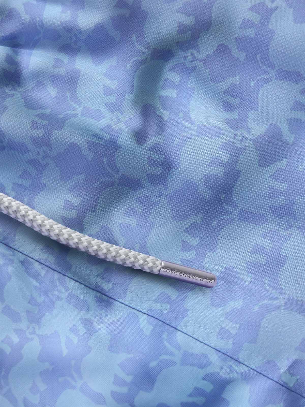 Close-up of blue elephant swimming shorts by love brand. Light blue swim shorts with elephant design.