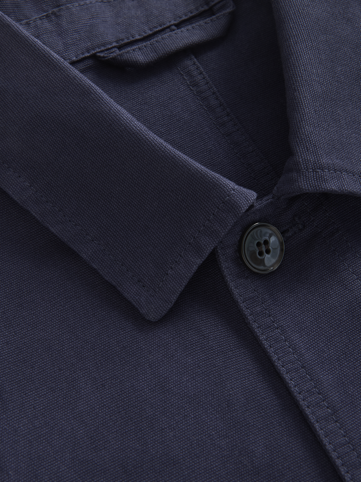 Close-up of a dark navy blue collared cotton jacket showing the collar, button, and fine fabric texture.