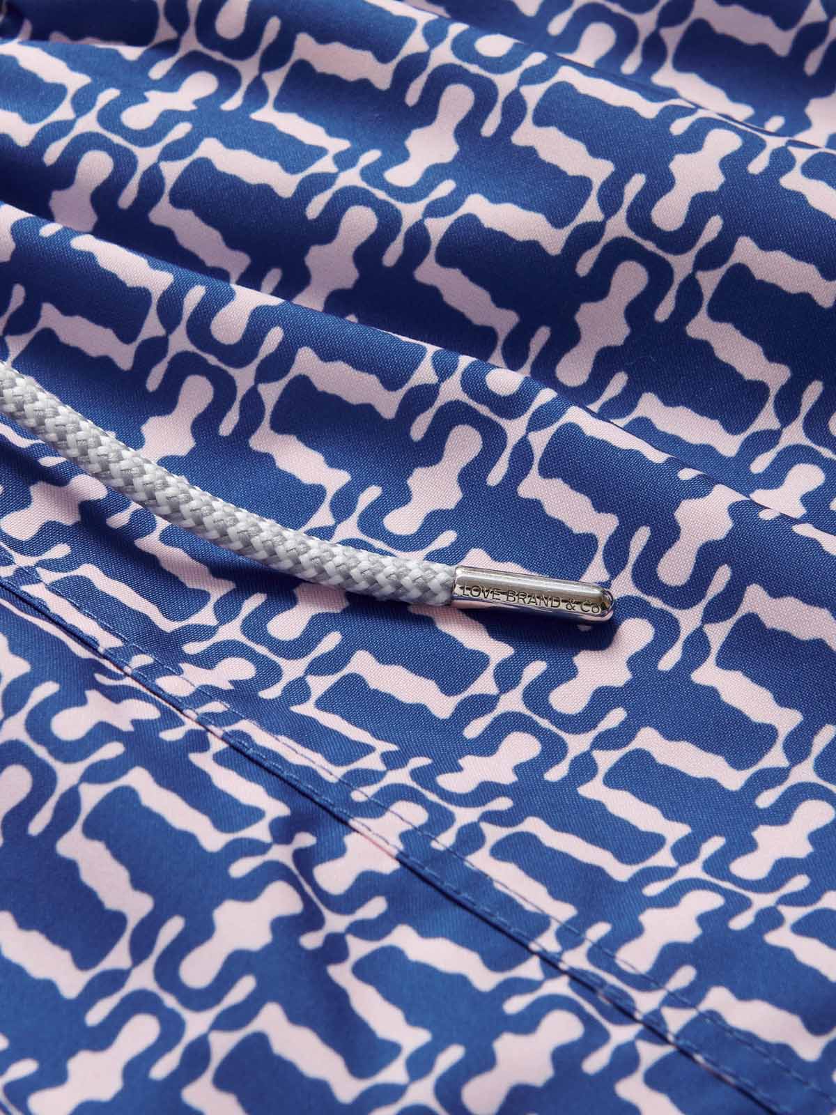 Close-up of Wilderness Staniel mens swim shorts. Patterned swim shorts featuring a pastel pink pattern on a blue background.