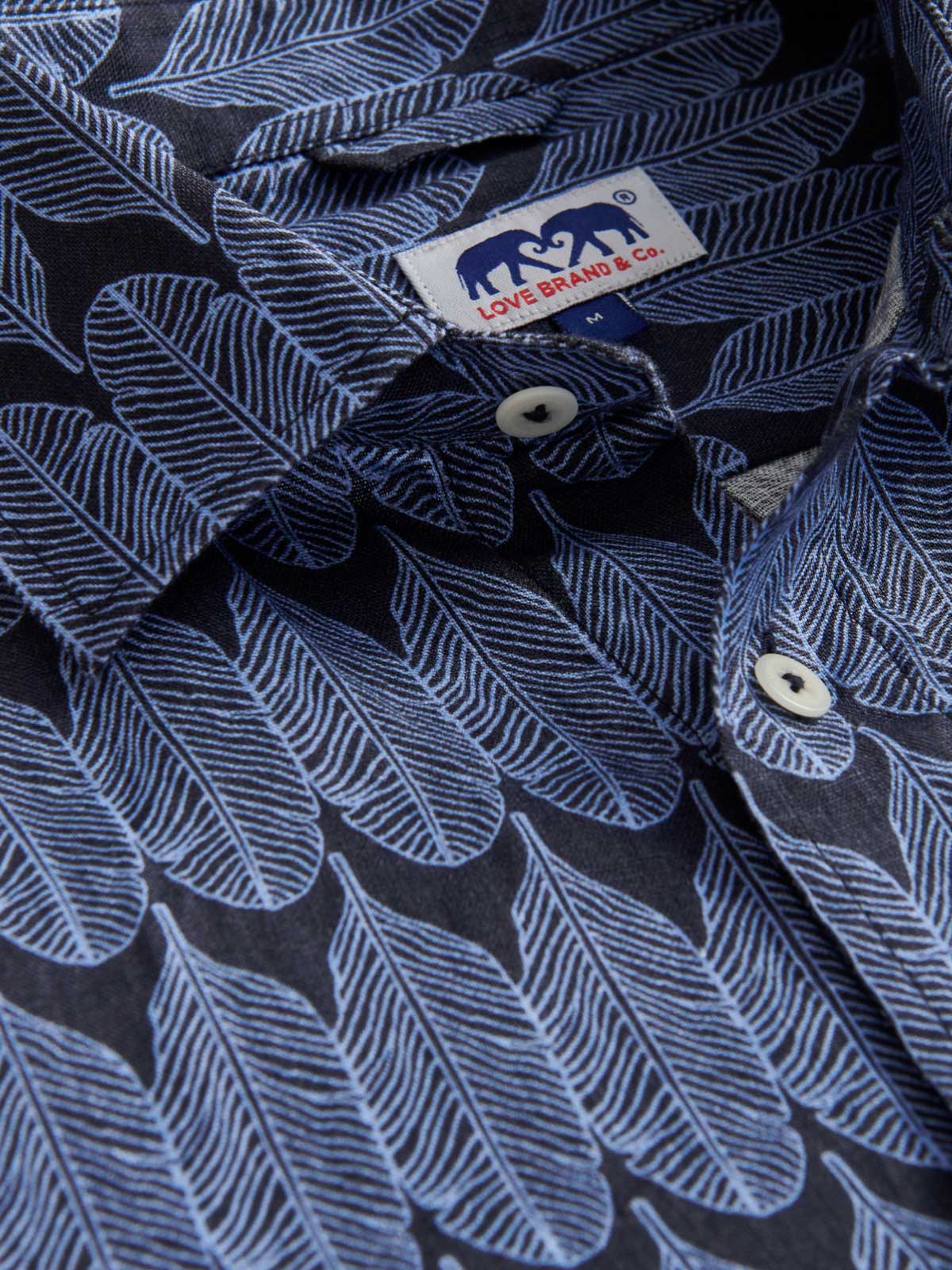 Close-up collar view of men's gone bananas abaco linen shirt. Blue tropical print shirt showing love brand label.