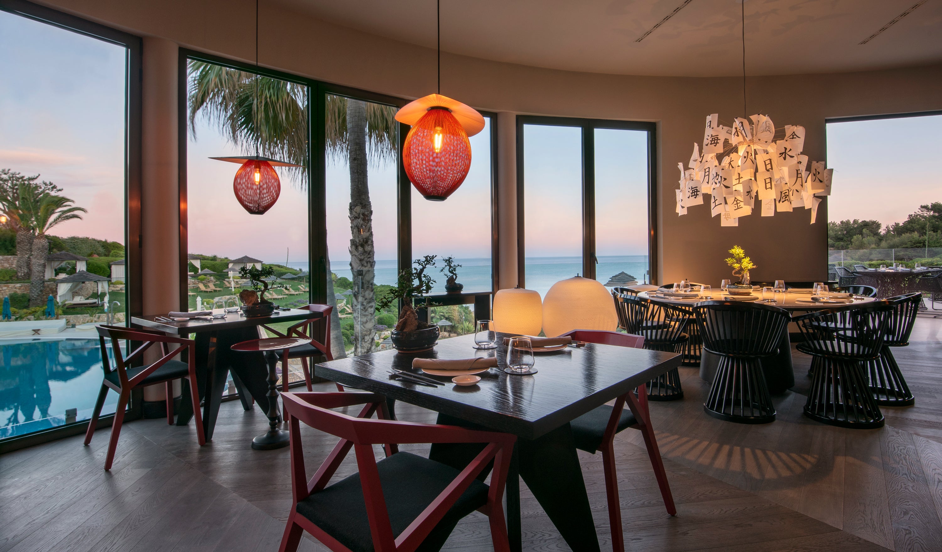 Modern restaurant interior with tables, chairs, and large windows overlooking a scenic view.