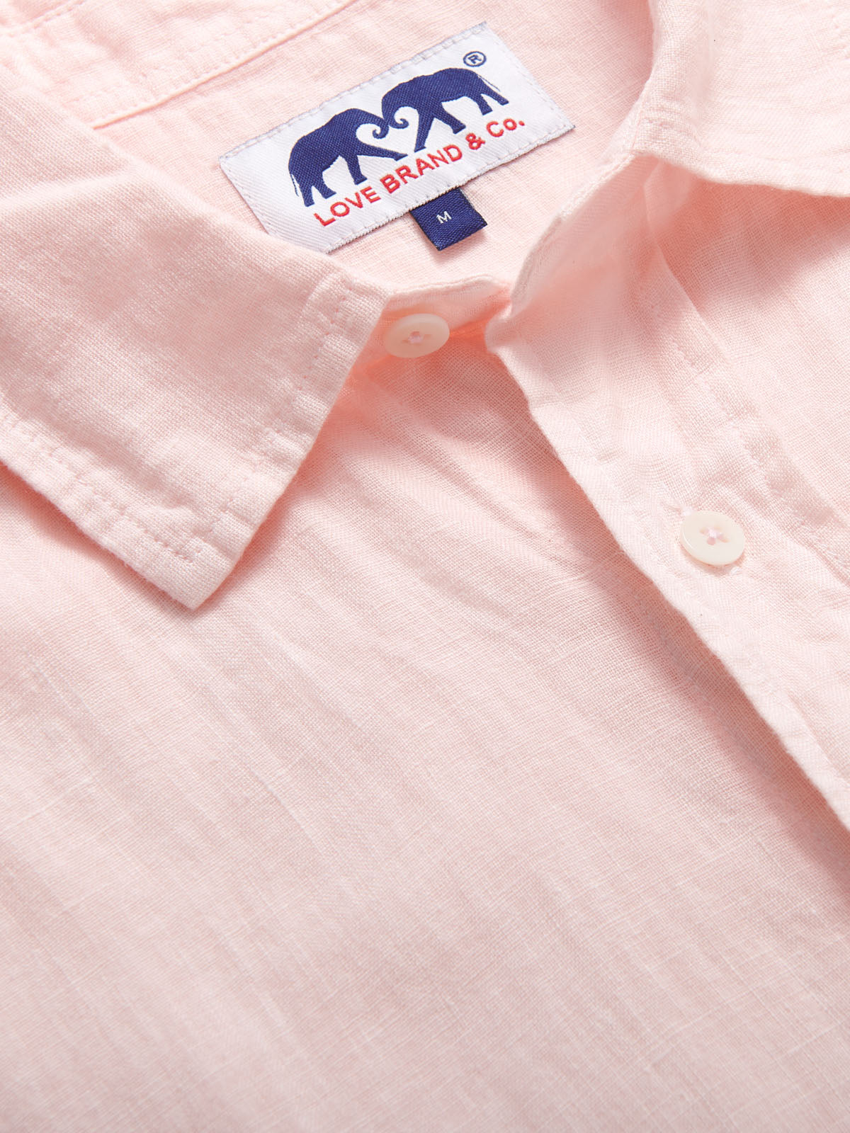 Pastel pink Manjack linen shirt for men, 100% linen, short-sleeved, lightweight, shown with detailed stitching and buttons.