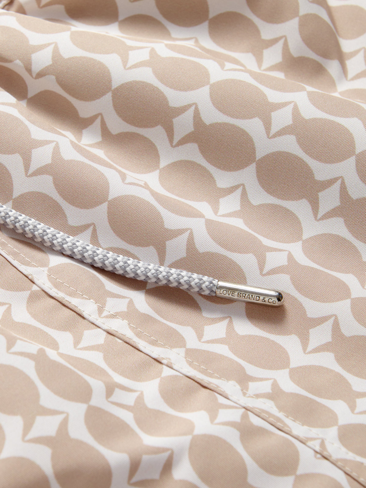 Luxury swim shorts details by Love Brand showcasing fish and pineapple pattern in brown and white.