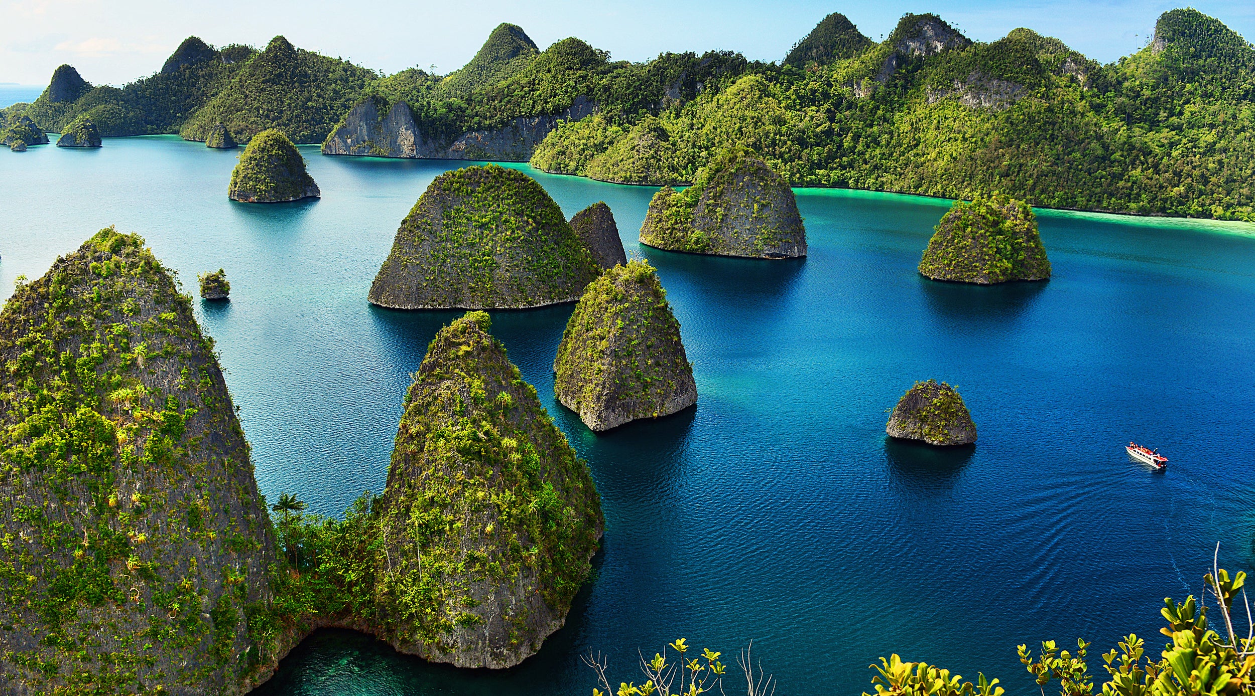 The lush green islands of Raja Ampat surrounded by clear blue water with a boat in the distance.
