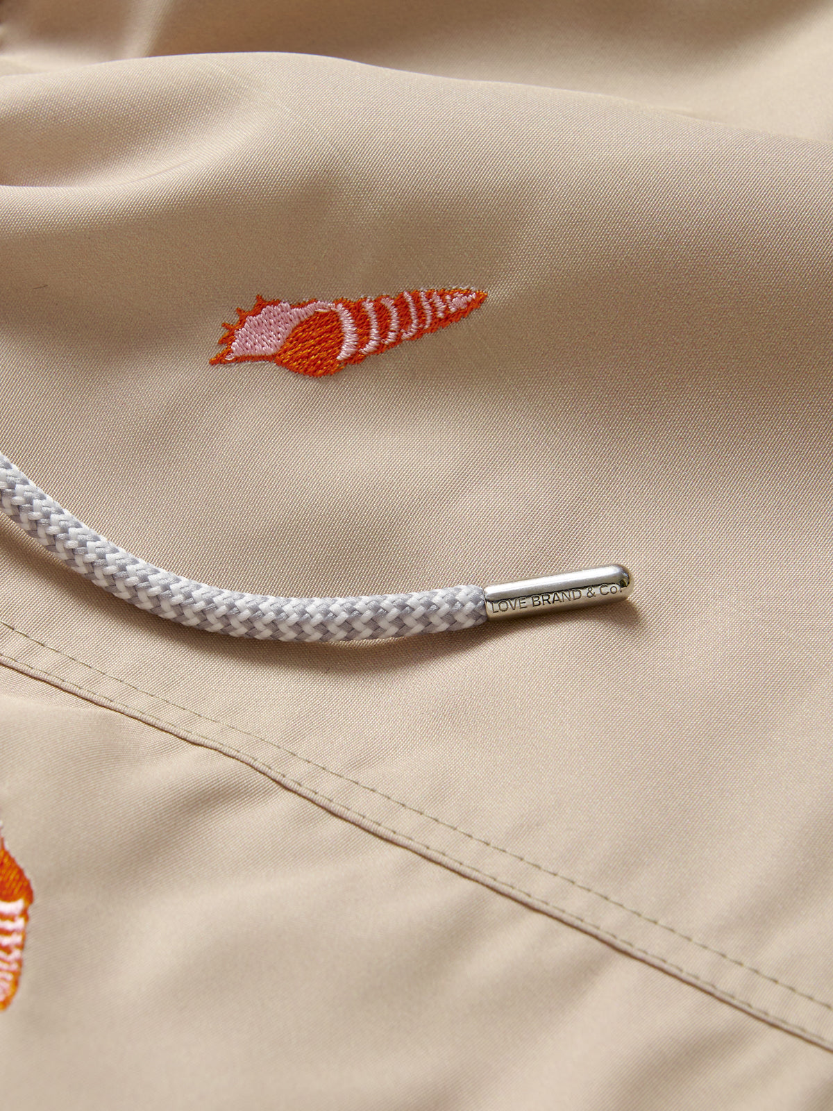 Detailed view of red embroidered conch shells on Shellebration Embroidered Staniel Swim Shorts.