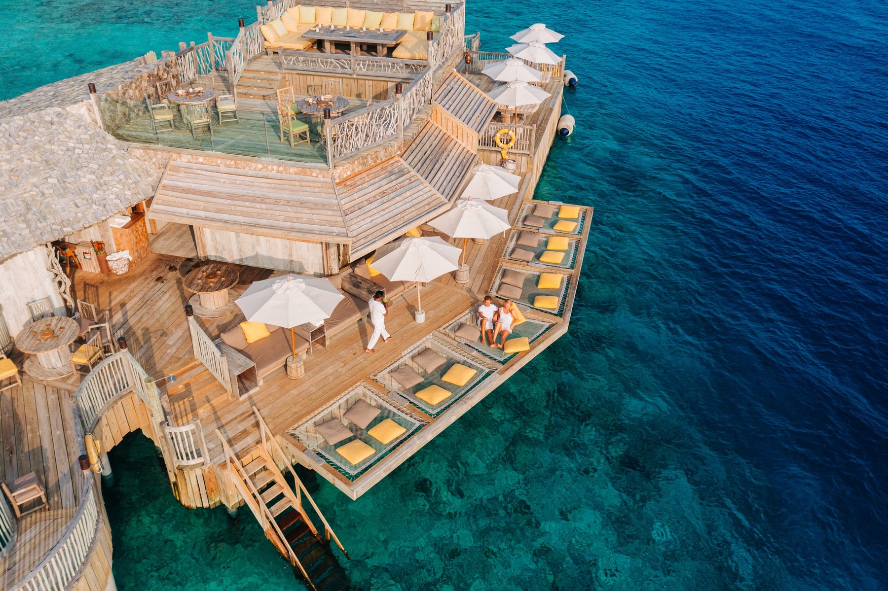Floating restaurant on water with wooden deck and umbrellas at Soneva Fushi