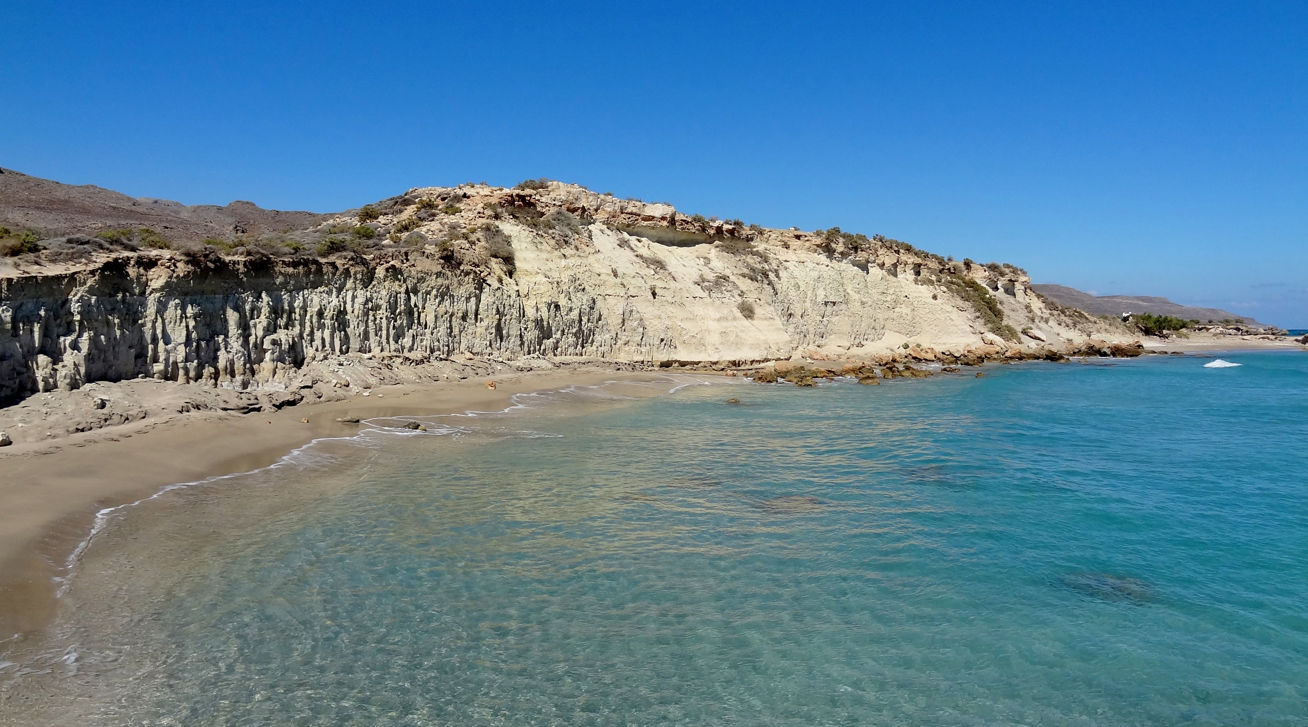 Xerokambos beach with clear blue water and cliffs under a bright blue sky