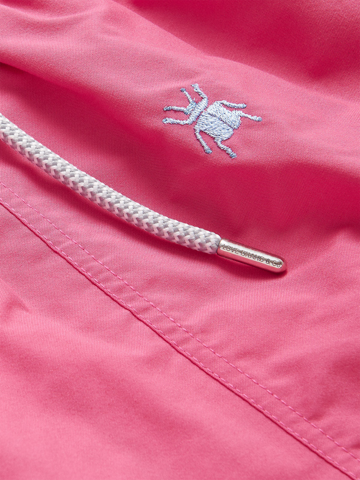 Close-up of Boys Beetle Bum Embroidered Staniel Swim Shorts in Ruby Red, showcasing the white embroidered tansy beetle and white drawstring with metallic tip.