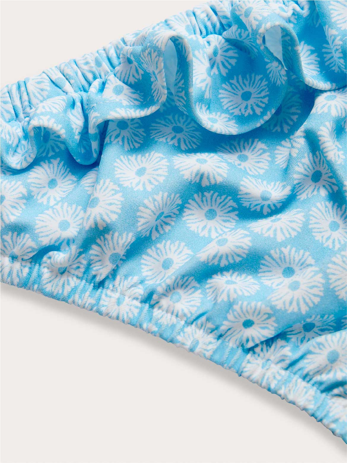 Close-up of blue bikini bottoms fabric with white floral pattern on a white background