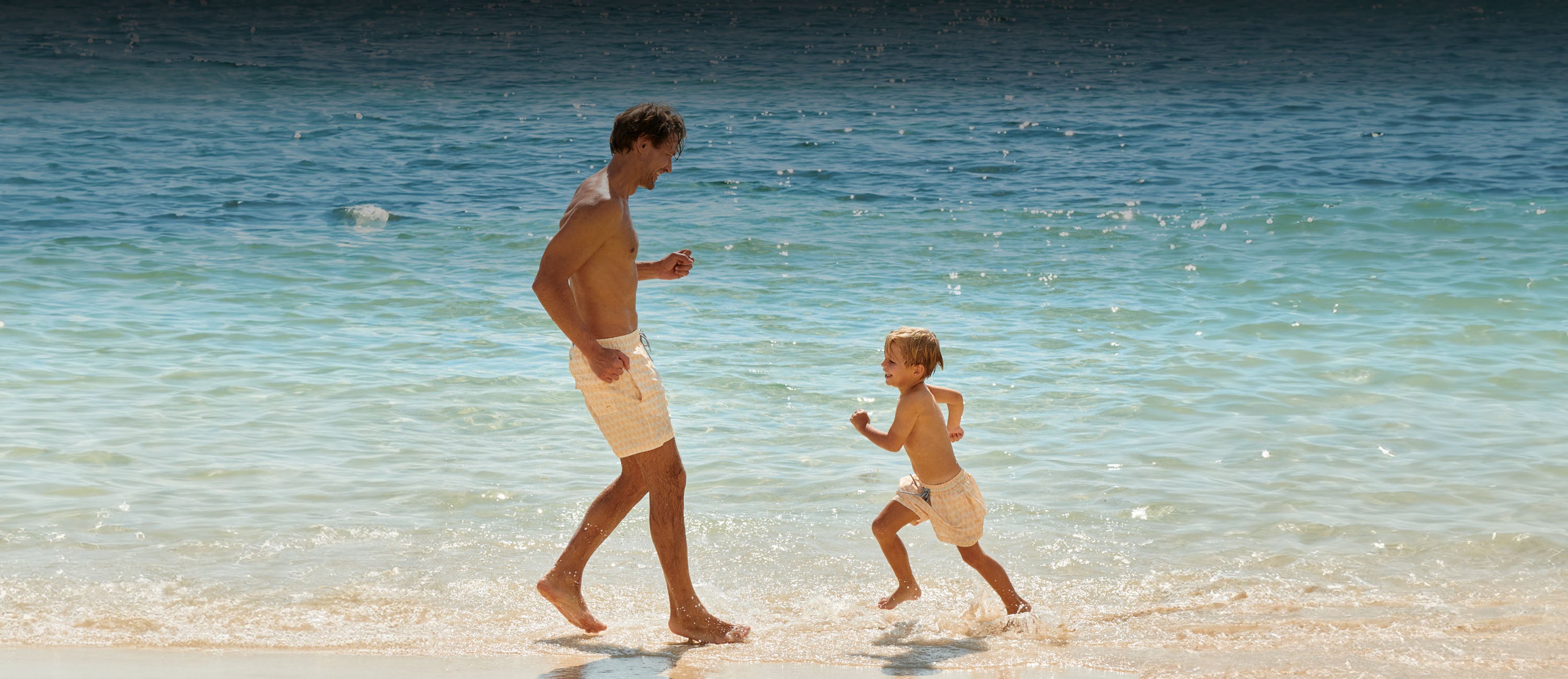 Man and child walking on a beach with clear blue water