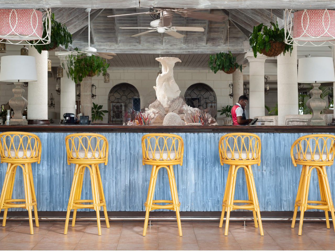 Bar area at the Coral Reef Club with yellow stools and a decorative fountain in the background.