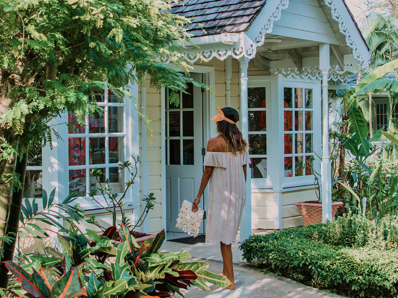 Woman in a white dress standing in front of a quaint boutique with greenery around.