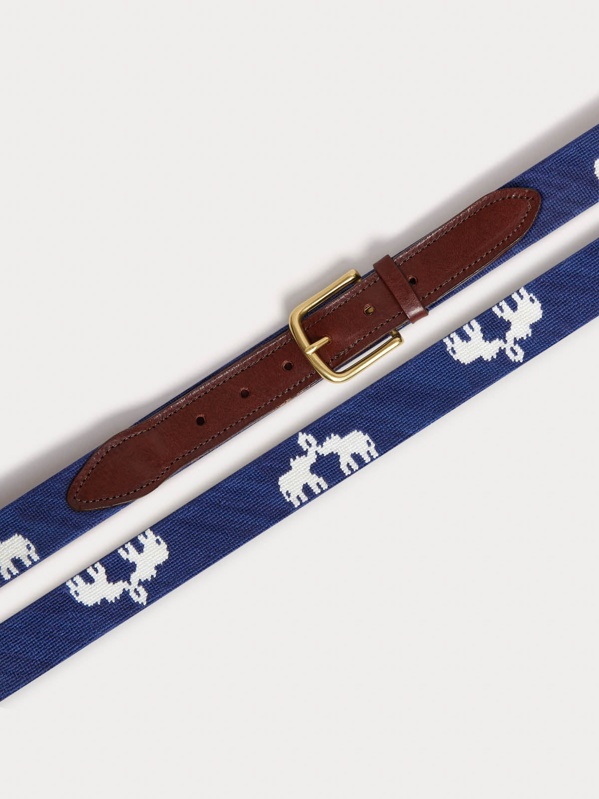 A woven belt with a navy blue base, white elephant pattern, and a brown leather keeper, shown on a light grey background.