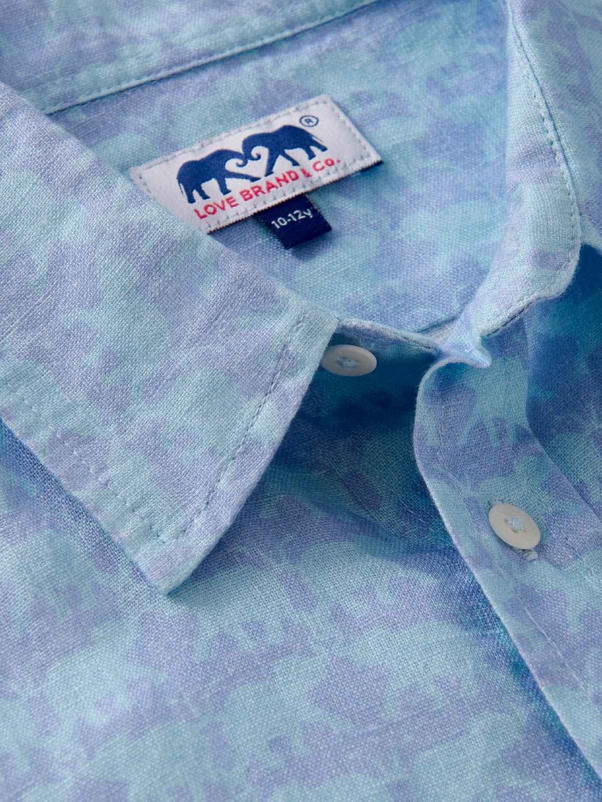 Close-up of a light blue shirt with a love brand label showing elephant design.
