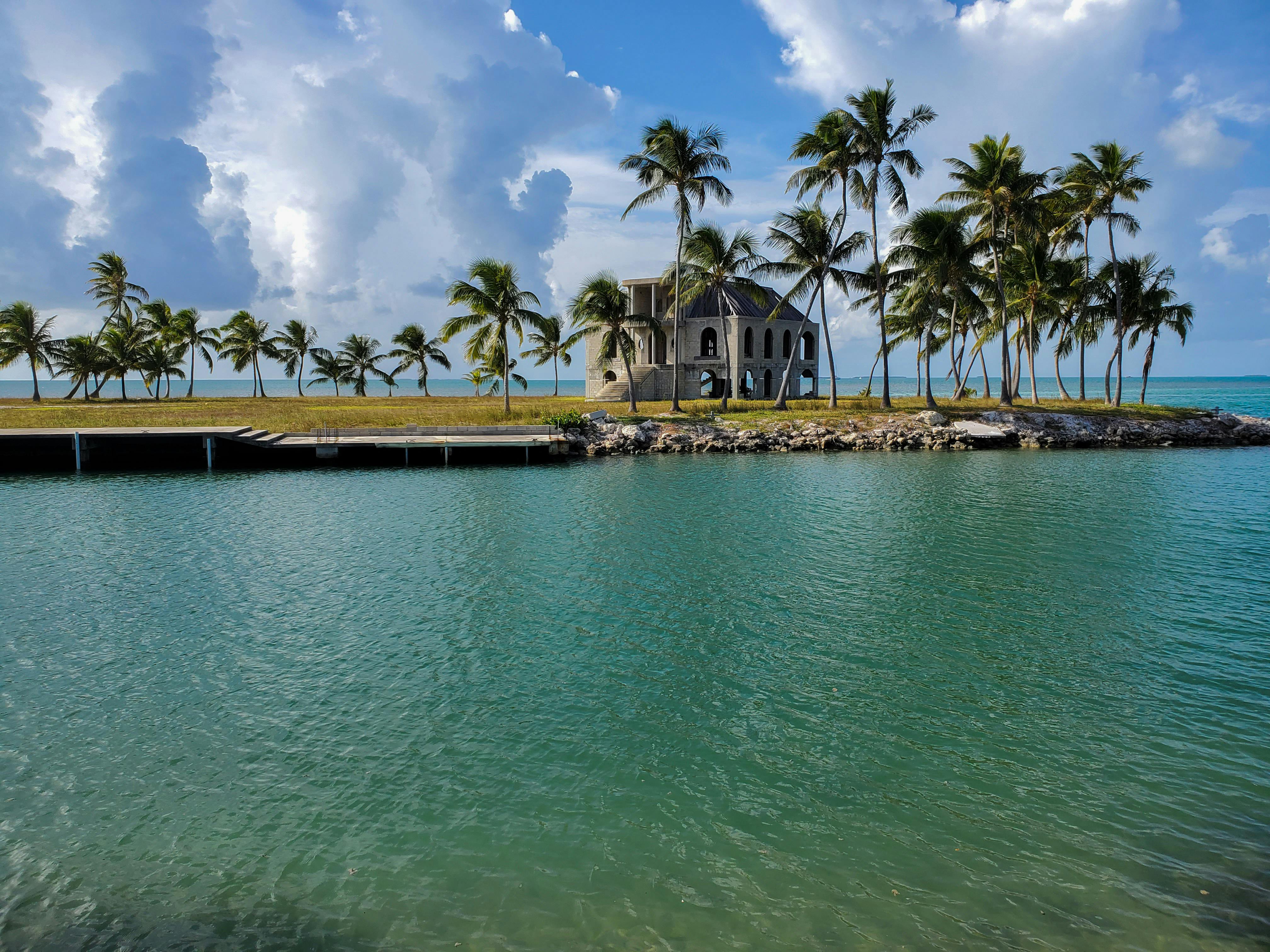 Tropical island with a house and palm trees near the water under a blue sky.