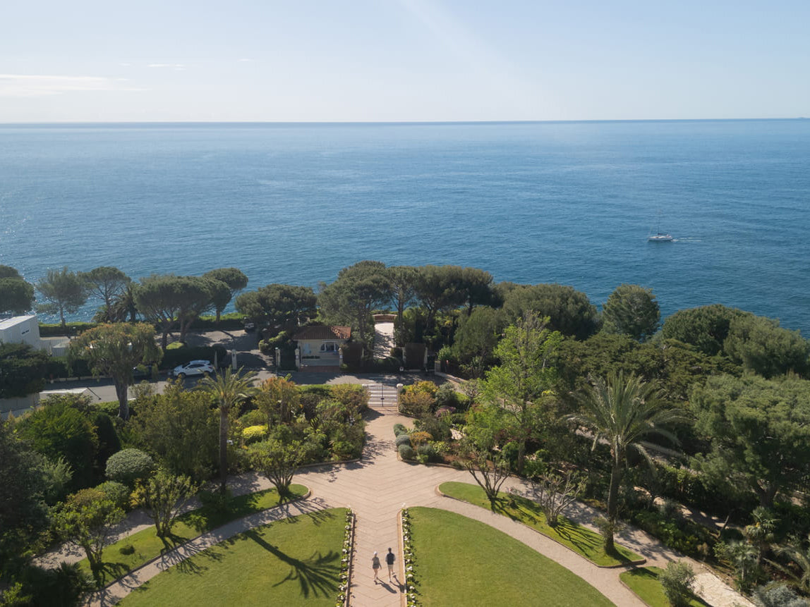 Aerial view of Grand-Hotel Du Cap-Ferrat with gardens and a path leading to the sea.