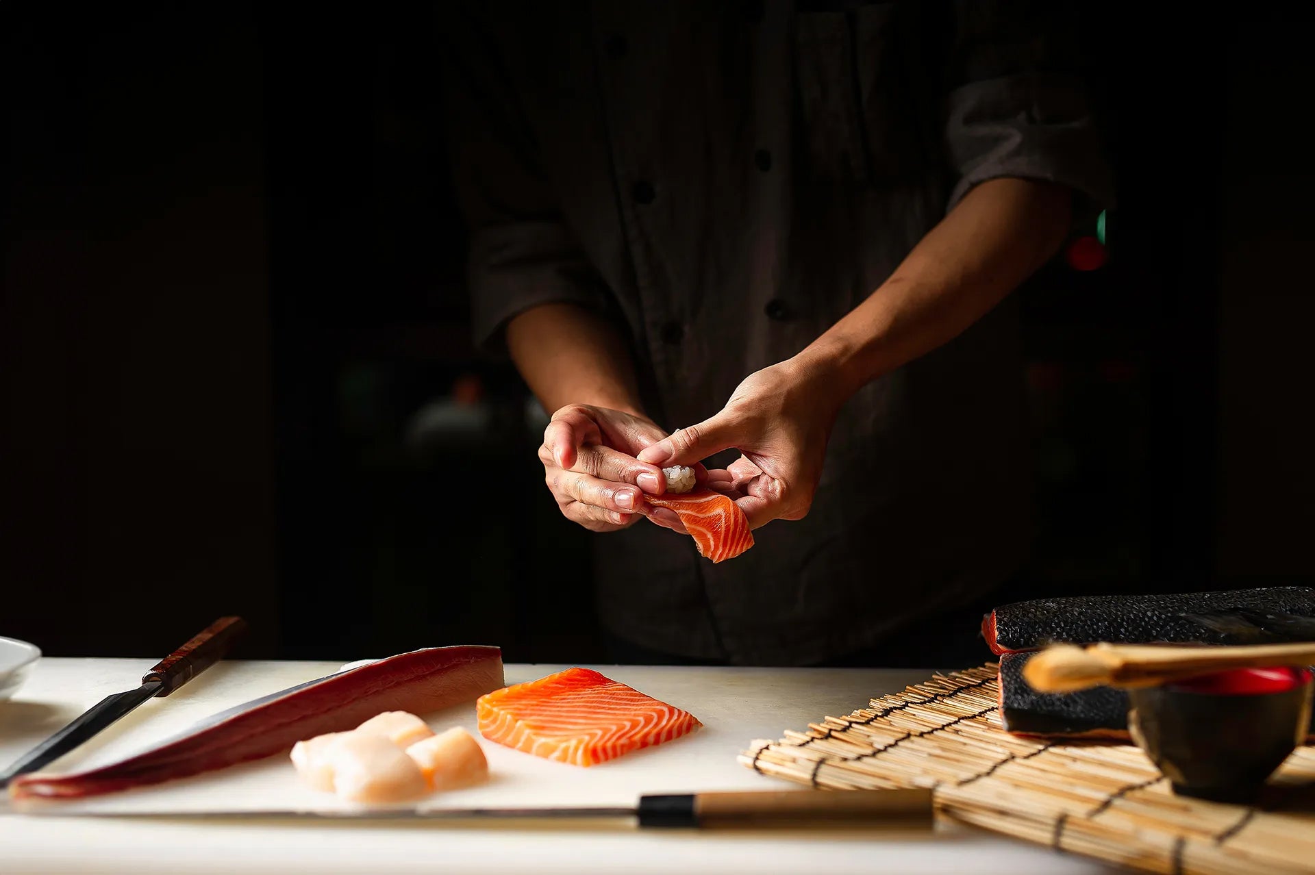 Person preparing sushi with ingredients on a dark background