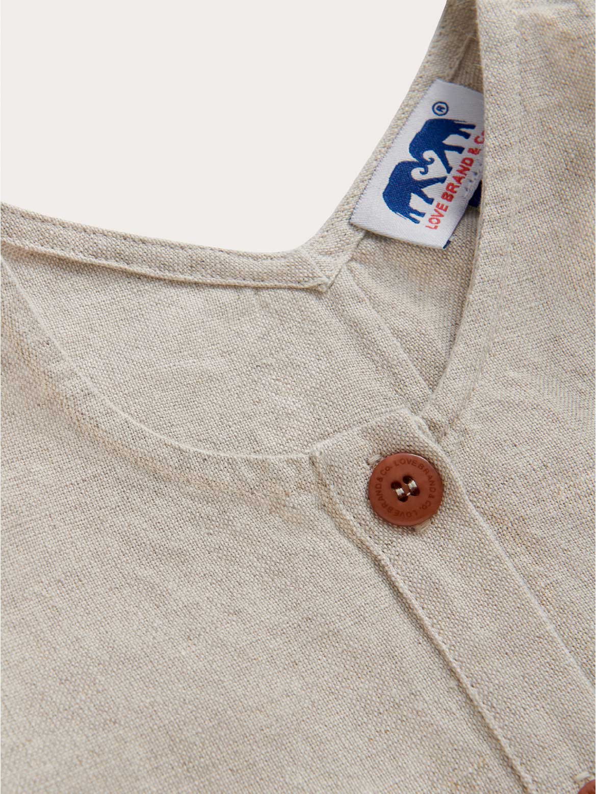 Close-up of a beige kids romper with a brown button and a visible love label.